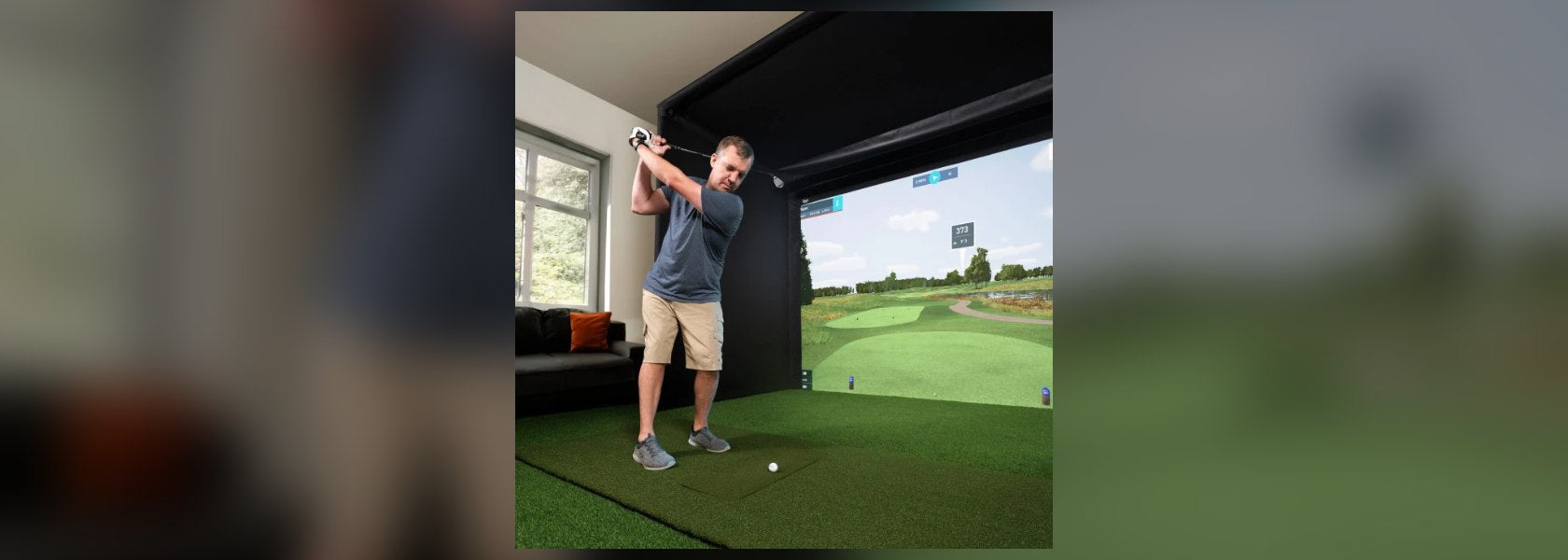 Golfer swinging a real club at a real golf ball inside a home golf simulator enclosure