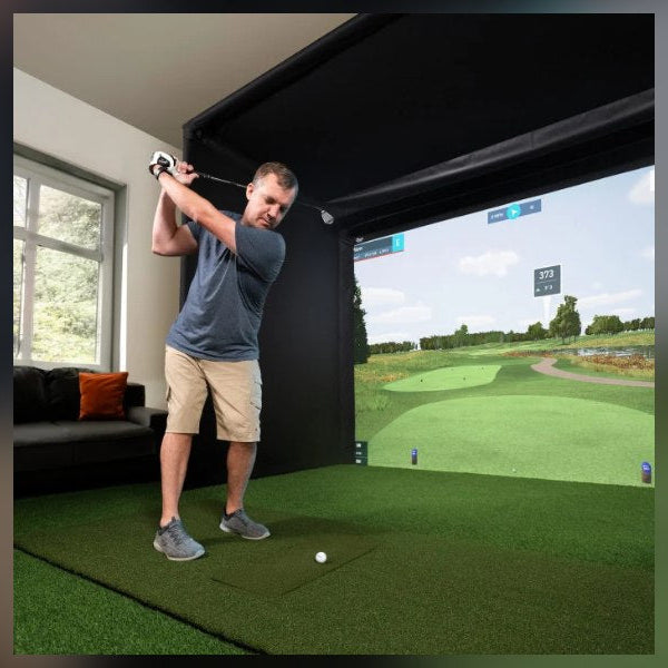 Golfer swinging a real club at a real golf ball inside a home golf simulator enclosure
