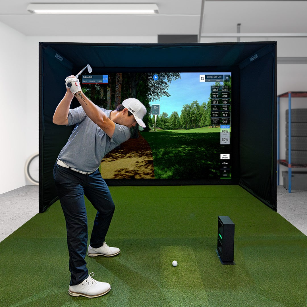 Golfer swinging in a garage golf simulator with the Uneekor EYE MINI LITE beside the ball