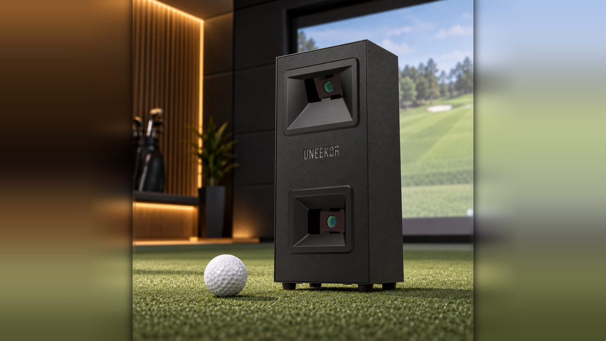 Uneekor Eye Mini Lite ground based golf launch monitor on turf next to a golf ball, with simulator screen in the background