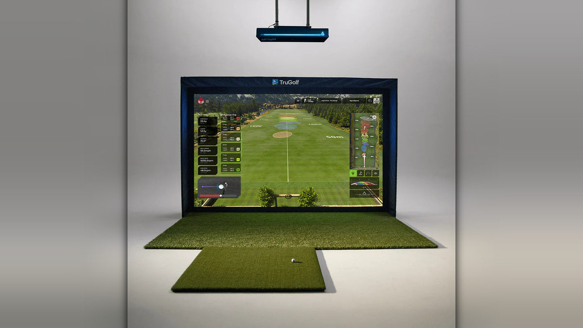 Indoor golf simulator setup with the TruGolf APOGEE launch monitor mounted on the ceiling above an impact screen showing a golf course, with hitting mats and a golf ball on the floor below