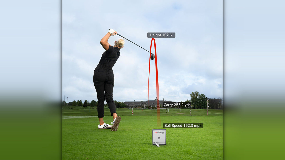 A female golfer finishing her swing on a driving range with the FlightScope Mevo Gen 2 on the turf in front of her, overlaid with a red ball flight trace showing height, carry distance and ball speed