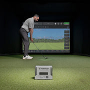 Man practicing golf swings in a simulator with a FlightScope Mevo+ device on the ground.