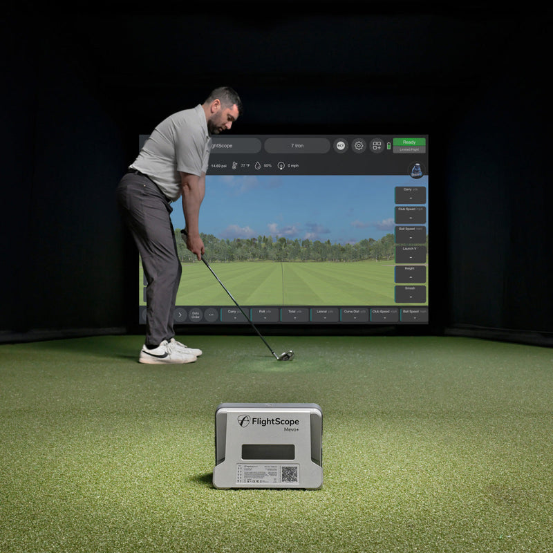 Man practicing golf swings in a simulator with a FlightScope Mevo+ device on the ground.