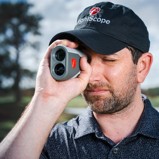 Man wearing a black cap with 'FlightScope' logo, holding a FlightScope i4 Rangefinder outdoors.