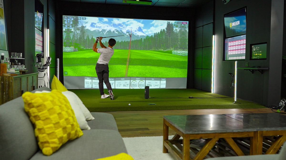 Golfer swinging in a residential golf simulator lounge with the Uneekor Eye Mini Lite, mountain course on screen and shot data displayed