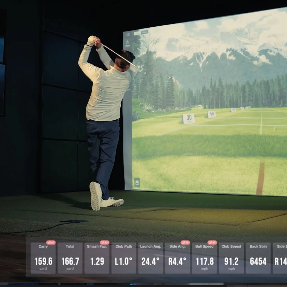 Golfer swinging in a Uneekor Eye XR golf simulator with mountain course on screen and live shot data displayed