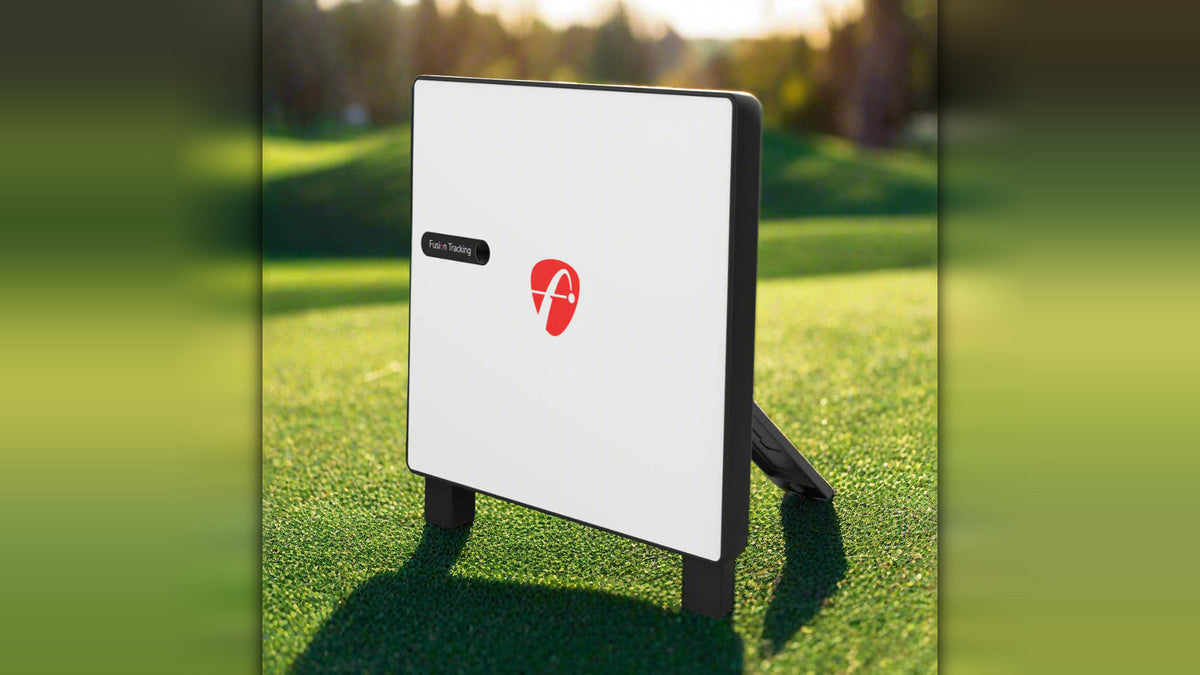 FlightScope X3C launch monitor viewed from the side, showing its white body with red logo and Fusion Tracking label, set on grass with a blurred golf course backdrop