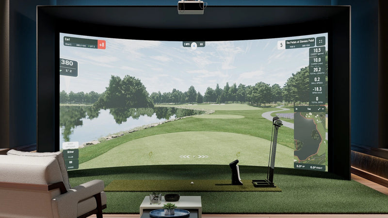 Home golf simulator room featuring Carl’s curved enclosure with a ceiling mounted projector displaying a golf course fairway, swing data overlays, seating, and a launch monitor