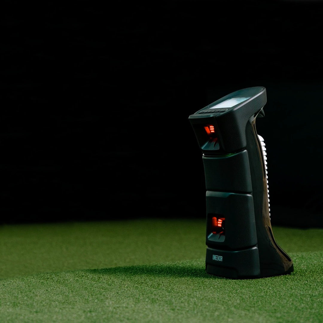 Uneekor EYE Mini launch monitor standing on artificial turf with infrared sensors lit