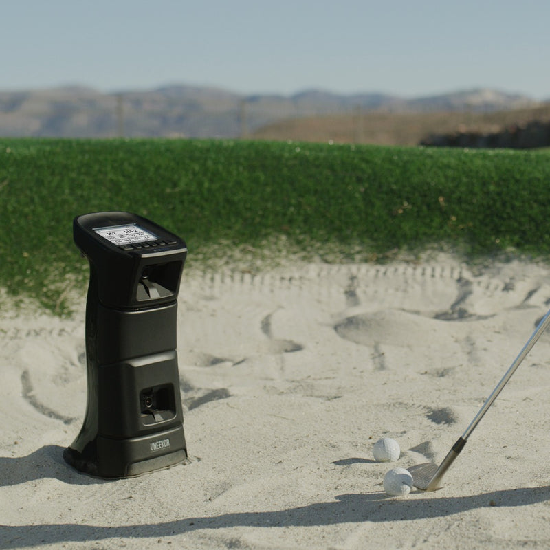 Uneekor EYE MINI launch monitor in a greenside bunker tracking a golfer's shot