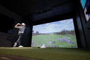 Golfer finishing a drive in an EYE XO2 simulator bay with a 410 yard shot shown on screen