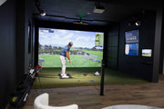 Golfer swinging in a Uneekor showroom golf simulator with the EYE XO2 mounted overhead and live data screens on the walls