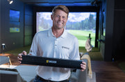 Uneekor team member holding the EYE XR launch monitor in a home golf simulator room
