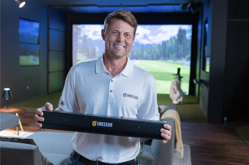 Uneekor team member holding the EYE XR launch monitor in a home golf simulator room